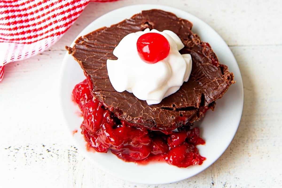 A decadent chocolate cake with a dollop of whipped cream and a juicy cherry on top.