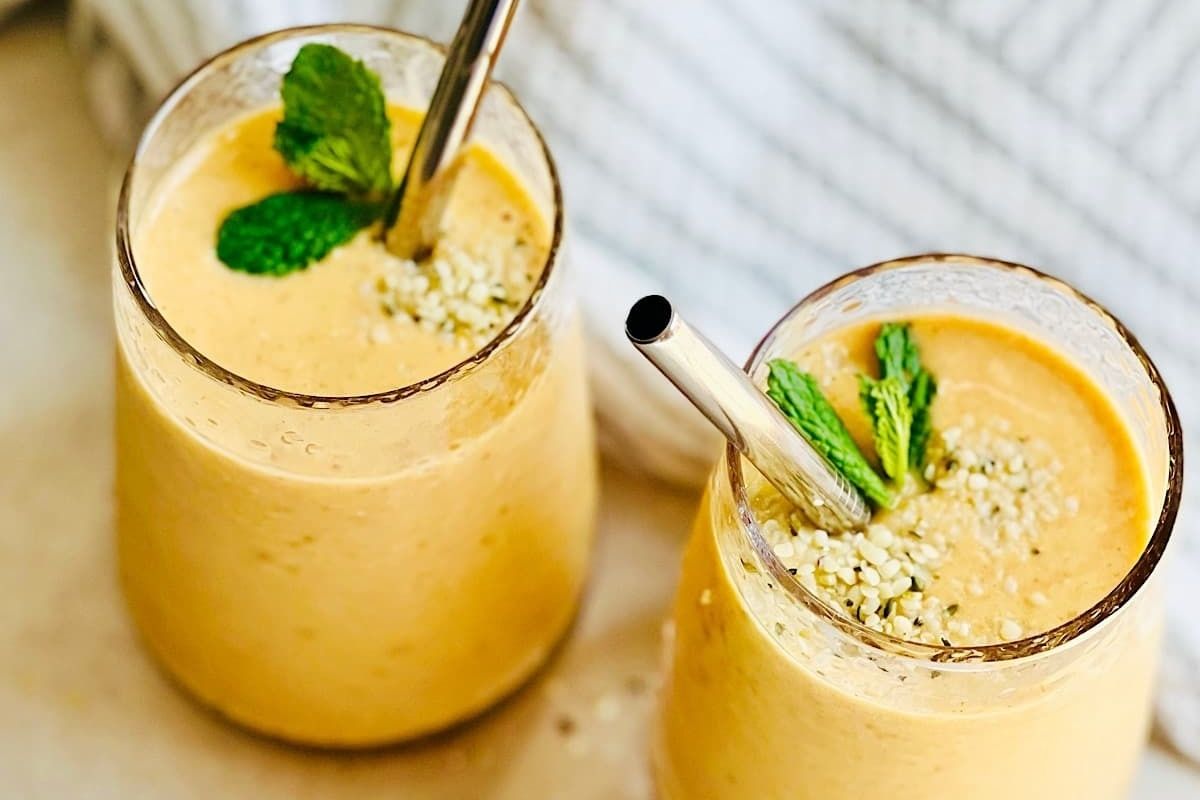 Two glasses of orange smoothie with mint leaves and pinwheel recipes.