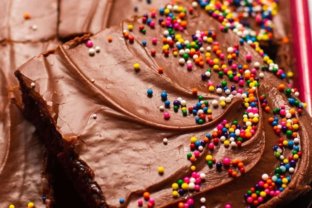 A close-up of chocolate brownies with a smooth chocolate frosting, topped with colorful sprinkles, just like the cherished recipes from Grandma.
