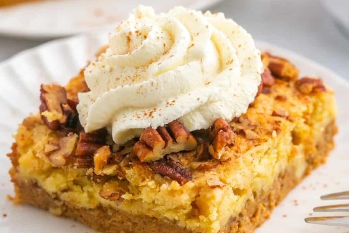 A slice of pumpkin cheesecake topped with whipped cream and pecans.