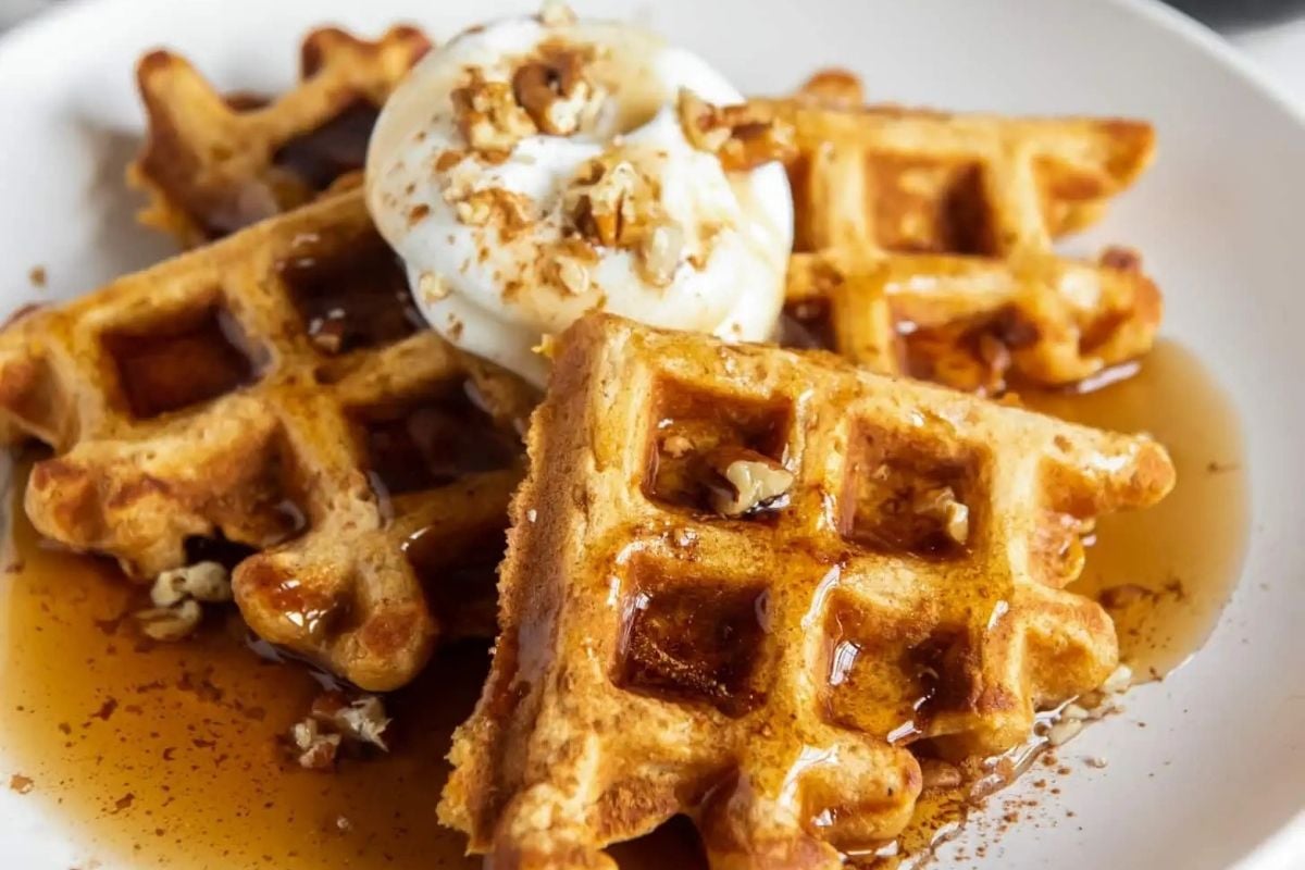 A plate of waffles topped with syrup and whipped cream.