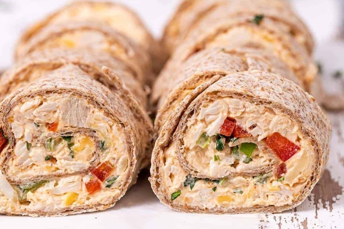 Sliced chicken and vegetable pinwheel wraps on a white surface.