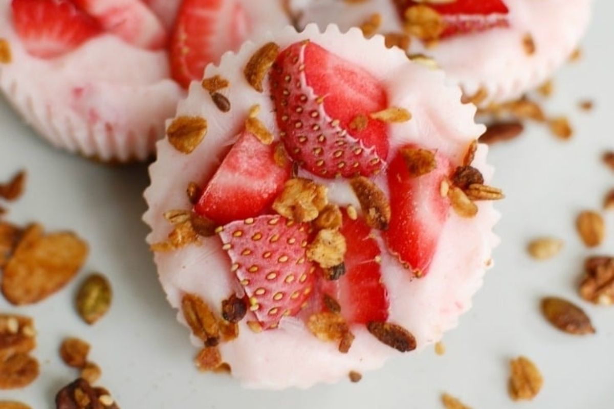 A yogurt cup topped with sliced strawberries and granola, with scattered granola pieces around it—perfect for fun and healthy Valentine's breakfasts for kids.
