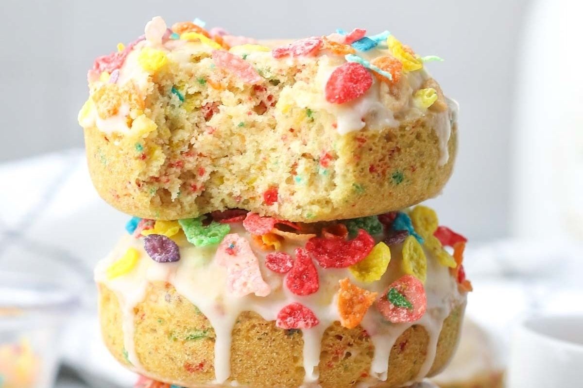 Two donuts topped with white icing and colorful fruity cereal, perfect for Valentine's breakfasts for kids—one even has a bite taken out!.