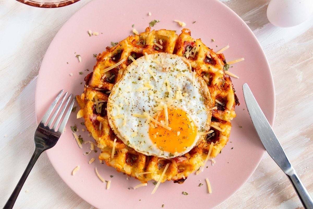 A delicious breakfast dish consisting of waffles topped with a perfectly fried egg, beautifully presented on a pink plate.