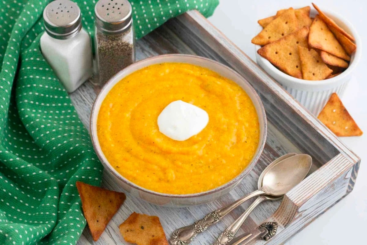 A creamy bowl of pumpkin soup, garnished with crackers and a dollop of sour cream.