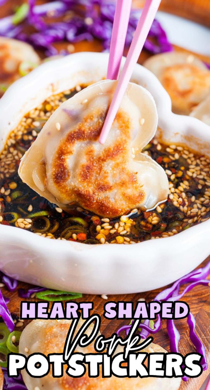 Heart shaped pork potstickers held with chopsticks, dipped in soy sauce, with text overlay and purple cabbage.