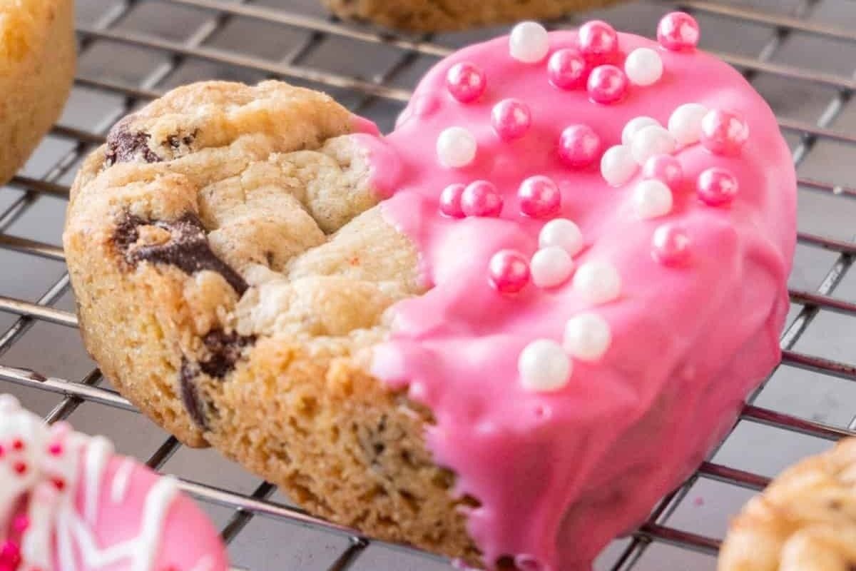 Heart-shaped cookies are delicately placed on a cooling rack, each adorned with a generous dollop of pink frosting.