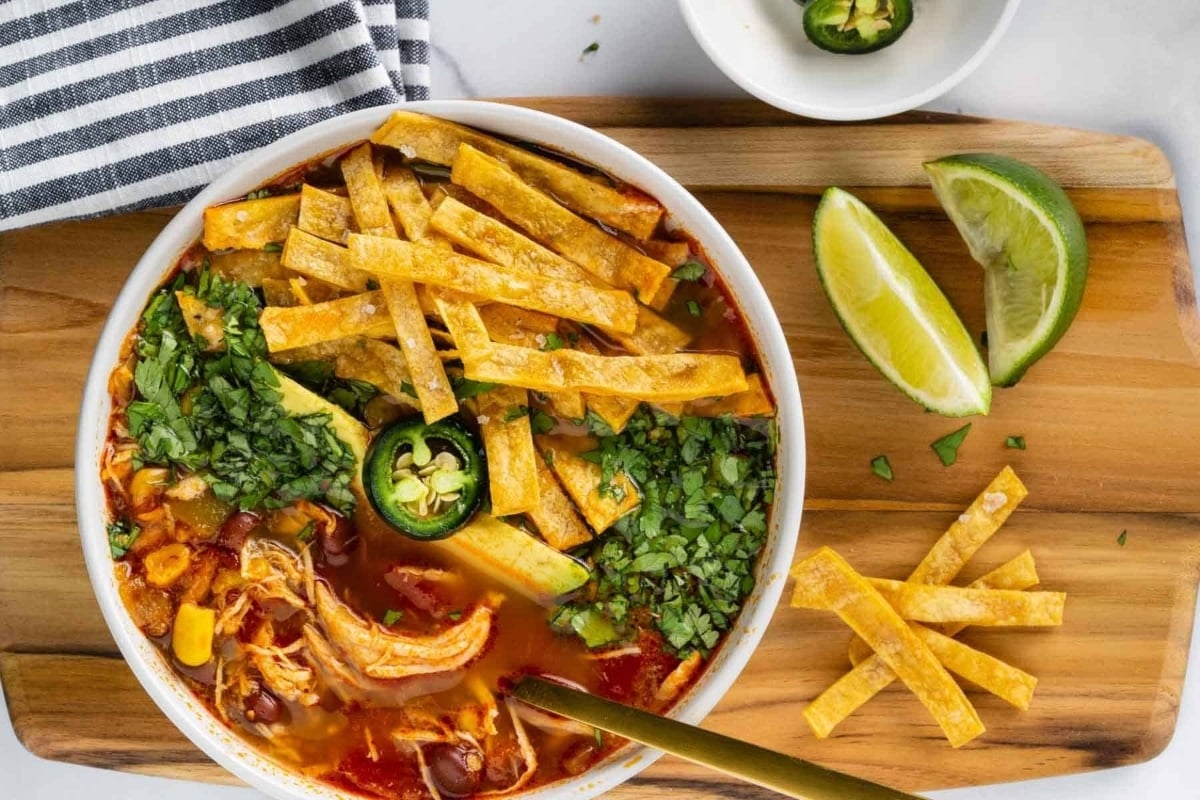 A bowl of chicken enchilada soup on a wooden cutting board, perfect for those craving a delicious and comforting meal.