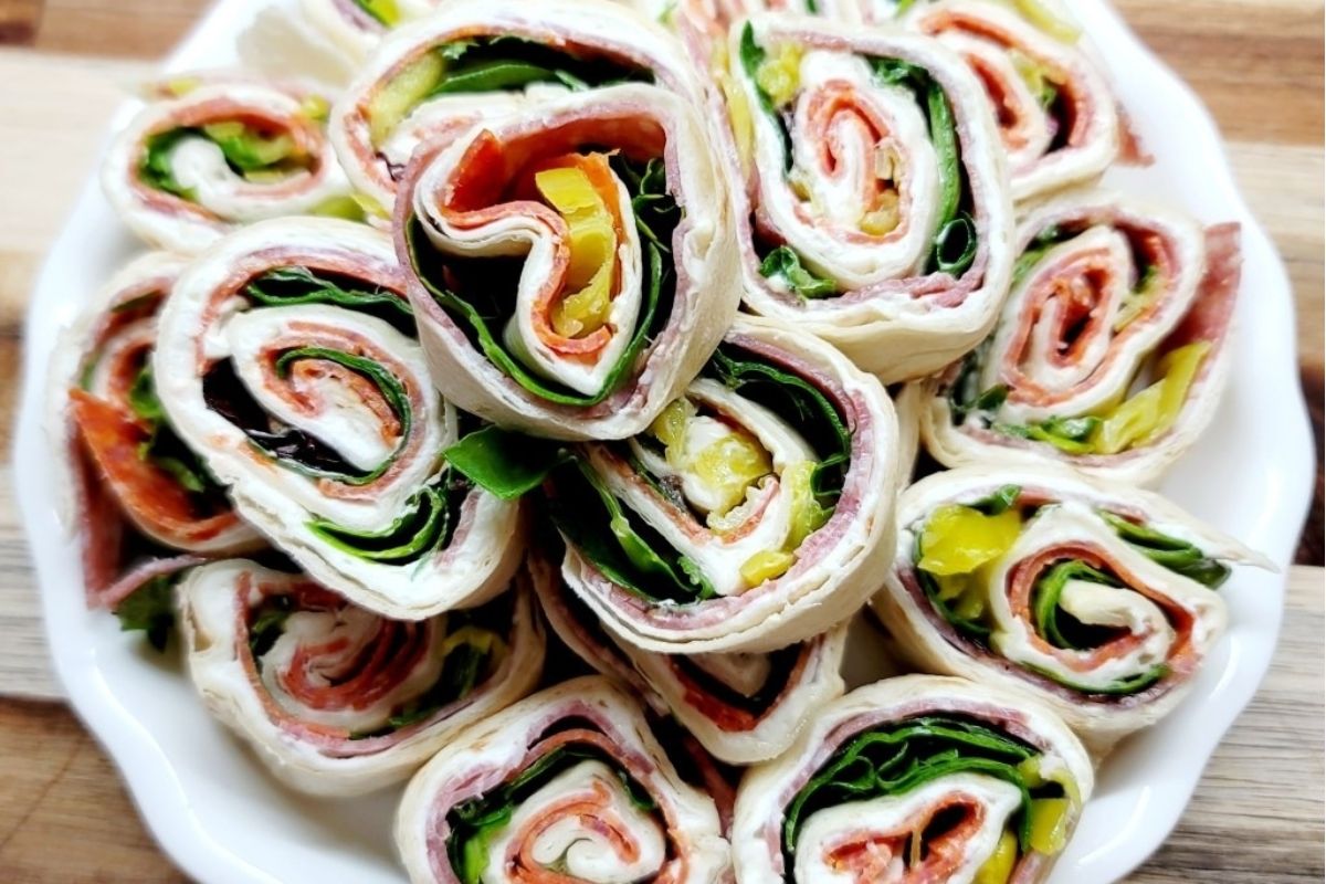 A plate of rolled tortilla pinwheel sandwiches filled with meats, cheese, greens, and sliced peppers—perfect for trying out new pinwheel recipes.