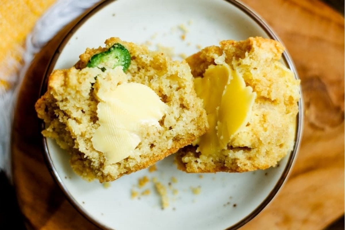 A savory muffin on a plate, sliced open with melting butter on top and crumbs around.