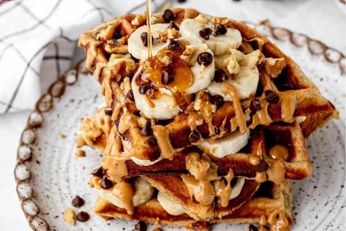 A stack of waffles smothered in peanut butter and topped with slices of bananas on a plate.