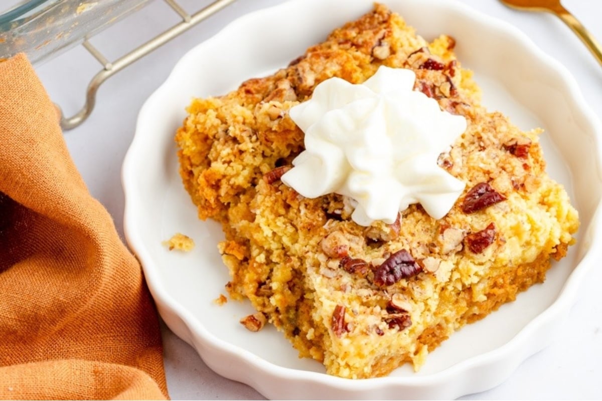 A delightful white plate with a piece of pumpkin bread adorned with a dollop of whipped cream.