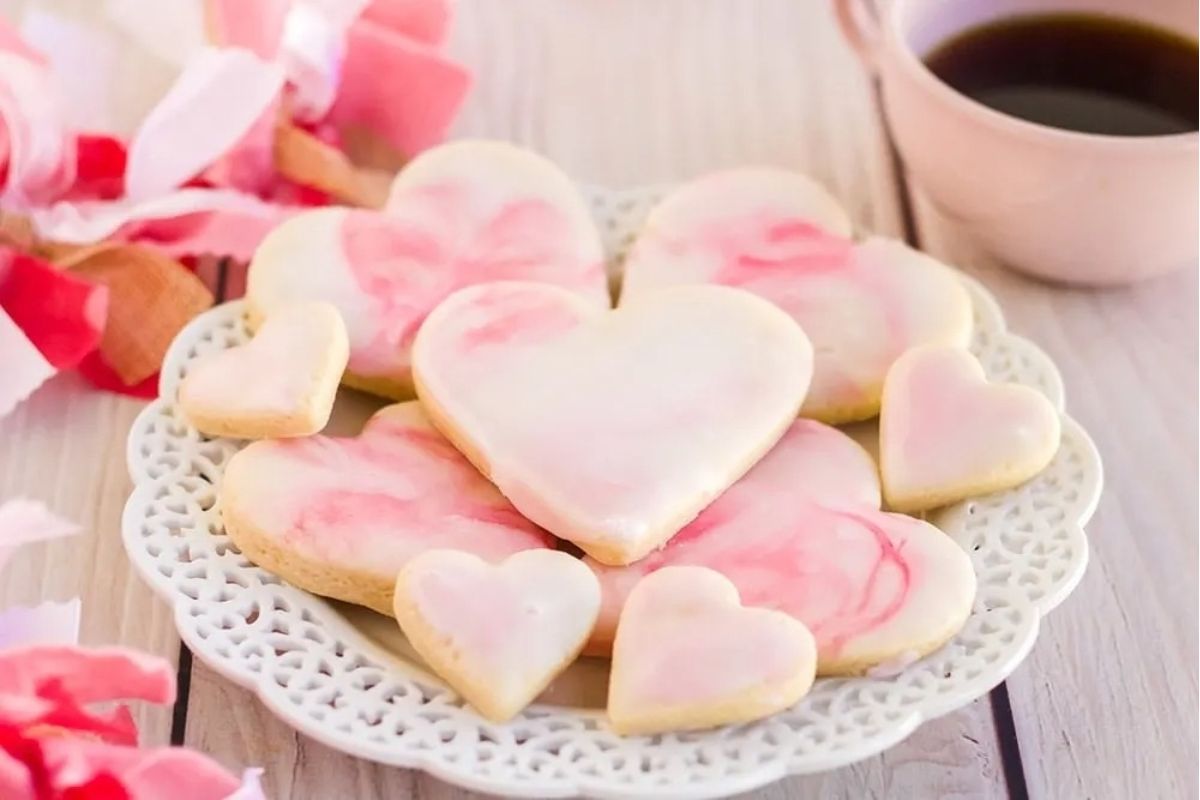 Valentine's day pink cookies on a plate with a cup of coffee.