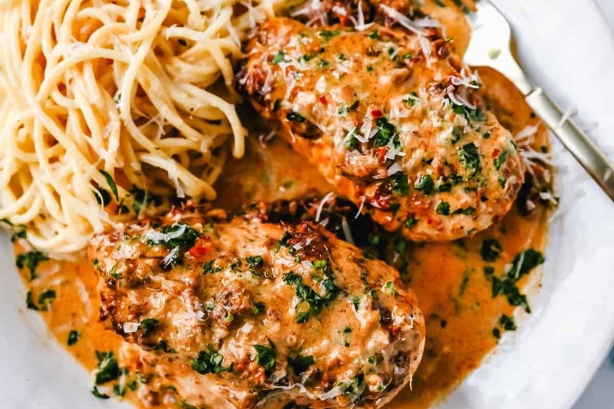 Chicken breasts in creamy sauce with herbs, served with spaghetti on a white plate and a fork on the side—a perfect Valentine's Date Night Dinner.