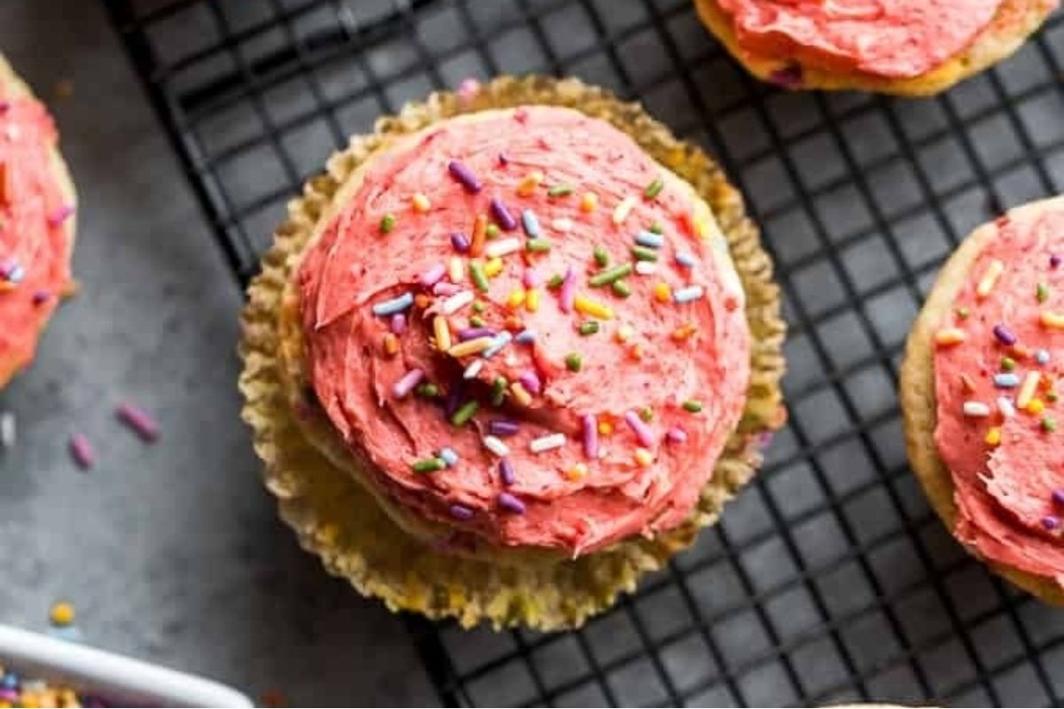 Pink frosted cupcakes with sprinkles on a cooling rack in a pink recipes theme.