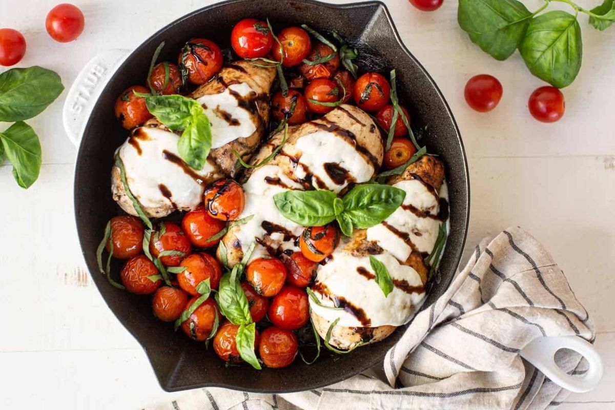 Balsamic Caprese chicken with mozzarella, cherry tomatoes, and basil in a skillet—perfect for a cozy Valentine's Date Night Dinner, served next to fresh basil and a towel.