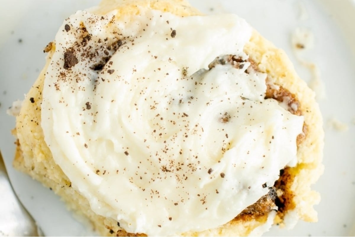 A cinnamon roll with icing and a fork on a plate.