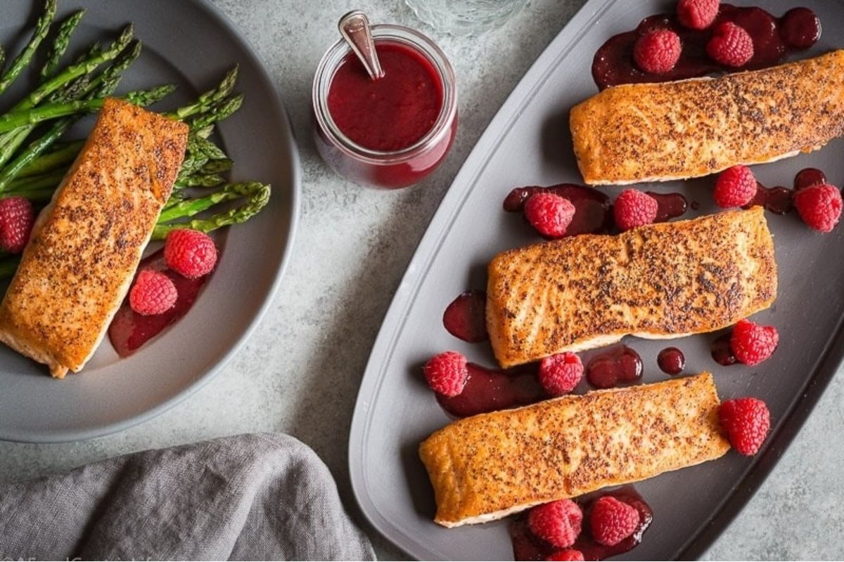 Three roasted salmon fillets with raspberries and sauce, plus asparagus on a separate plate—an elegant overhead view perfect for a Valentine's Date Night Dinner.