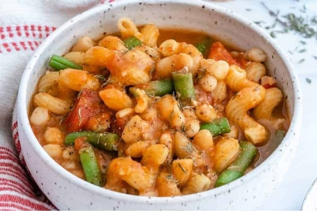 A bowl of pasta with tomato based sauce and green beans.
