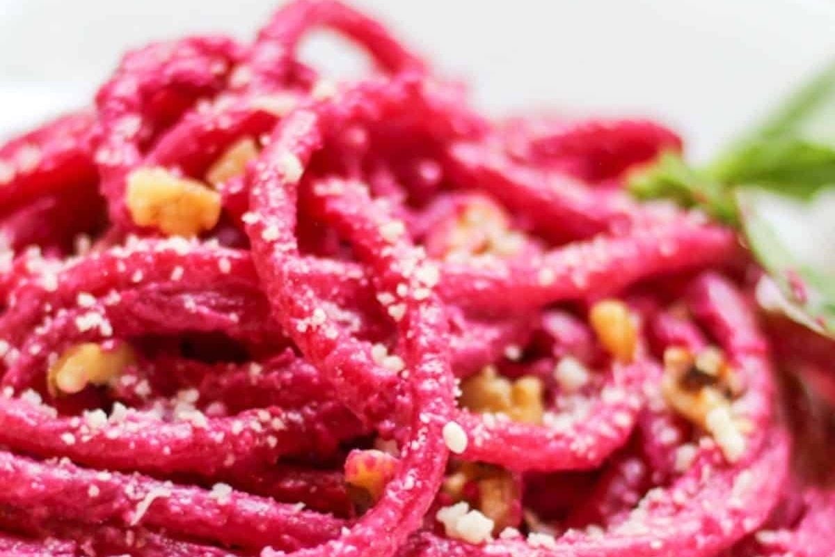 Close-up of bright pink beet pasta topped with crumbled nuts and grated cheese, garnished with herbs—an eye-catching dish perfect for a Valentine's Date Night Dinner.