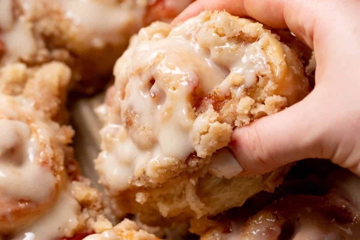 A hand holding a plate of mouthwatering cinnamon rolls with icing, showcasing the delectable results of following tantalizing cinnamon roll recipes.