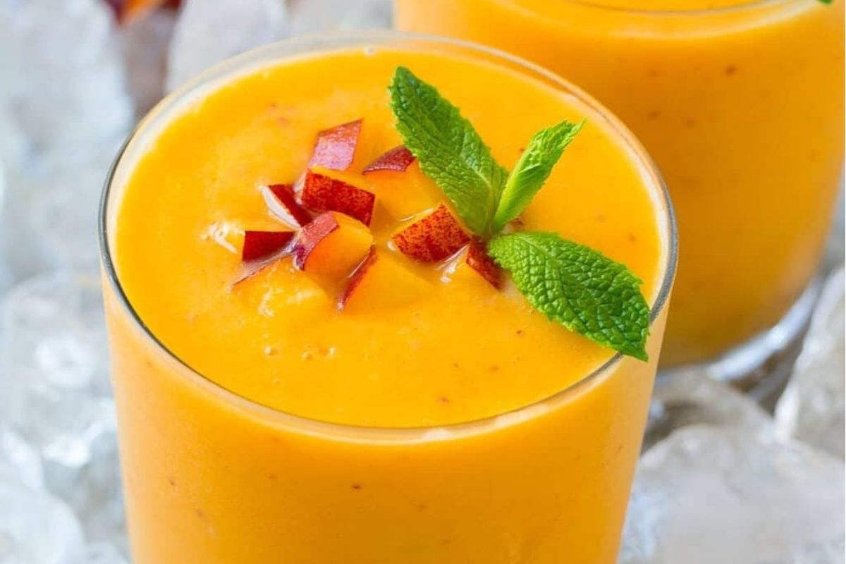 Two glasses of peach smoothie with mint leaves and pinwheel recipes.