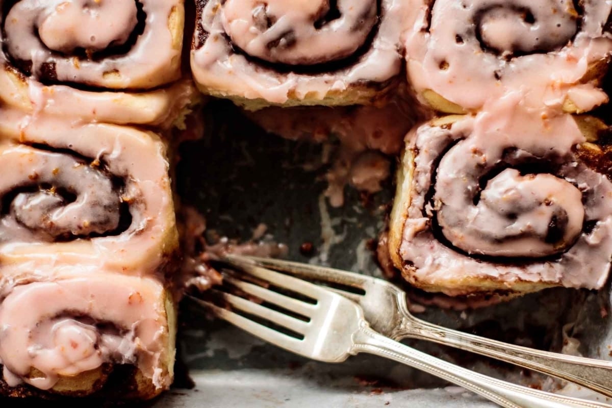 A pan of mouthwatering cinnamon rolls with icing and a fork, perfect for indulging in a homemade treat.