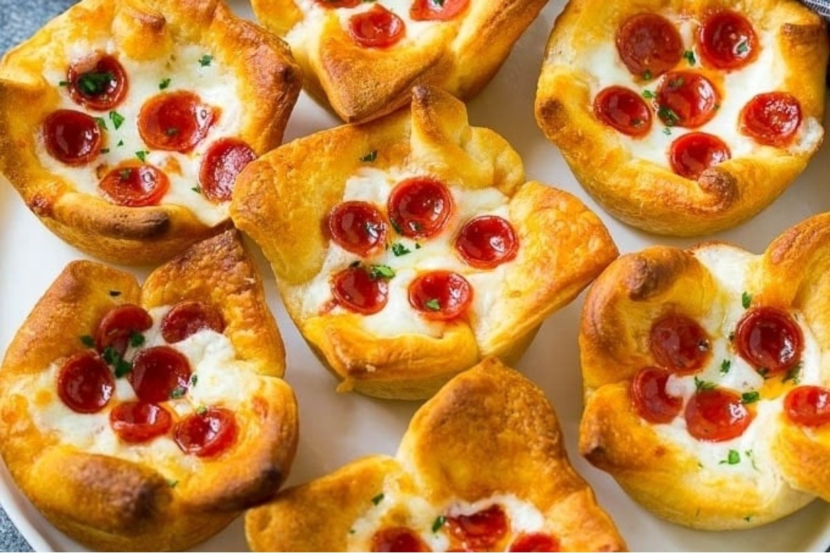 Six savory muffins topped with melted cheese and cherry tomatoes, garnished with parsley on a white plate.