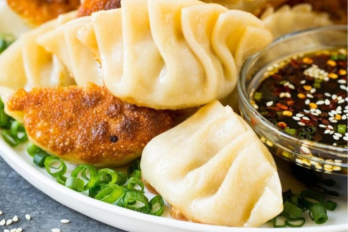 A plate of pan-fried dumplings with green onions and a bowl of soy dipping sauce with sesame seeds—perfect for adding to your collection of Lunar New Year recipes.