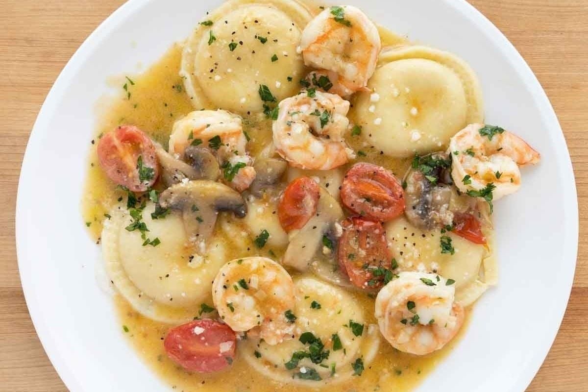 Explore this delightful dish made with shrimp ravioli, mushrooms, and tomatoes beautifully presented on a white plate.