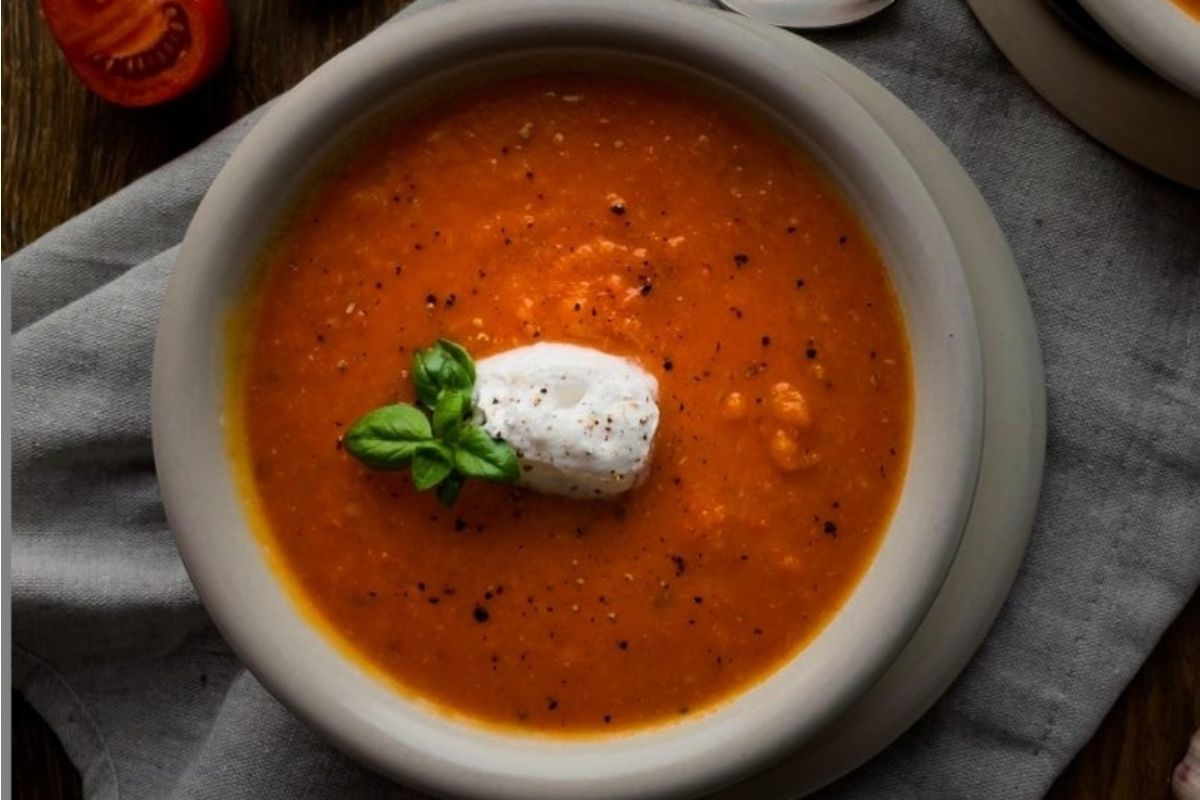 A bowl of tomato soup with sour cream and basil, perfect for those craving a flavorful tomato-based soup.