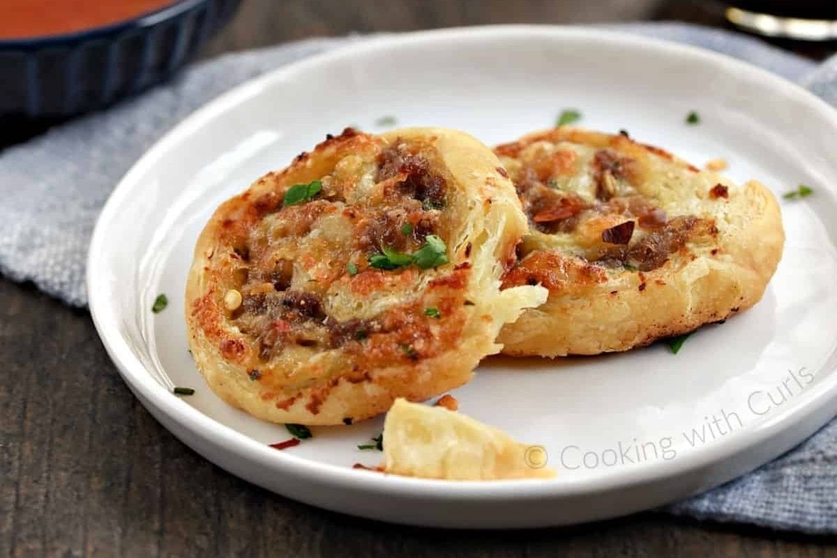 Two puff pastry pinwheels with melted cheese and herbs on a white plate—perfect for trying out your favorite pinwheel recipes.