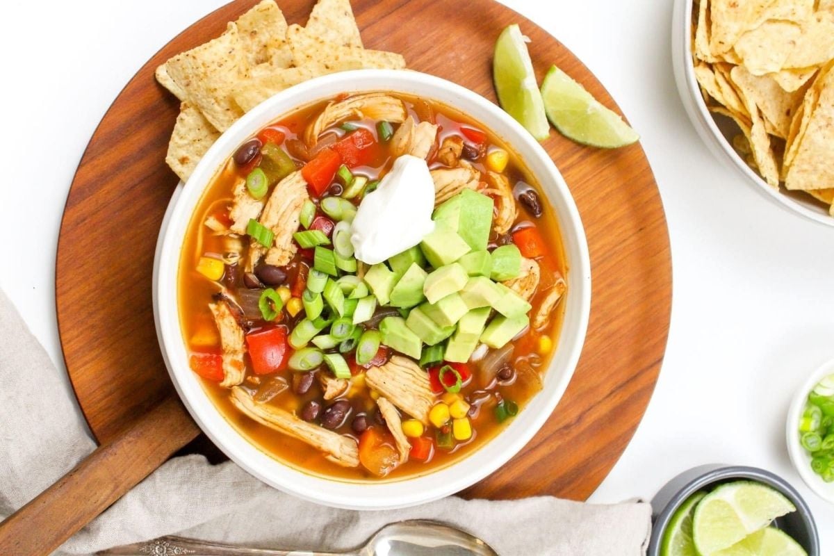 A wholesome bowl of slow cooker mexican chicken soup topped with tortilla chips and sour cream.