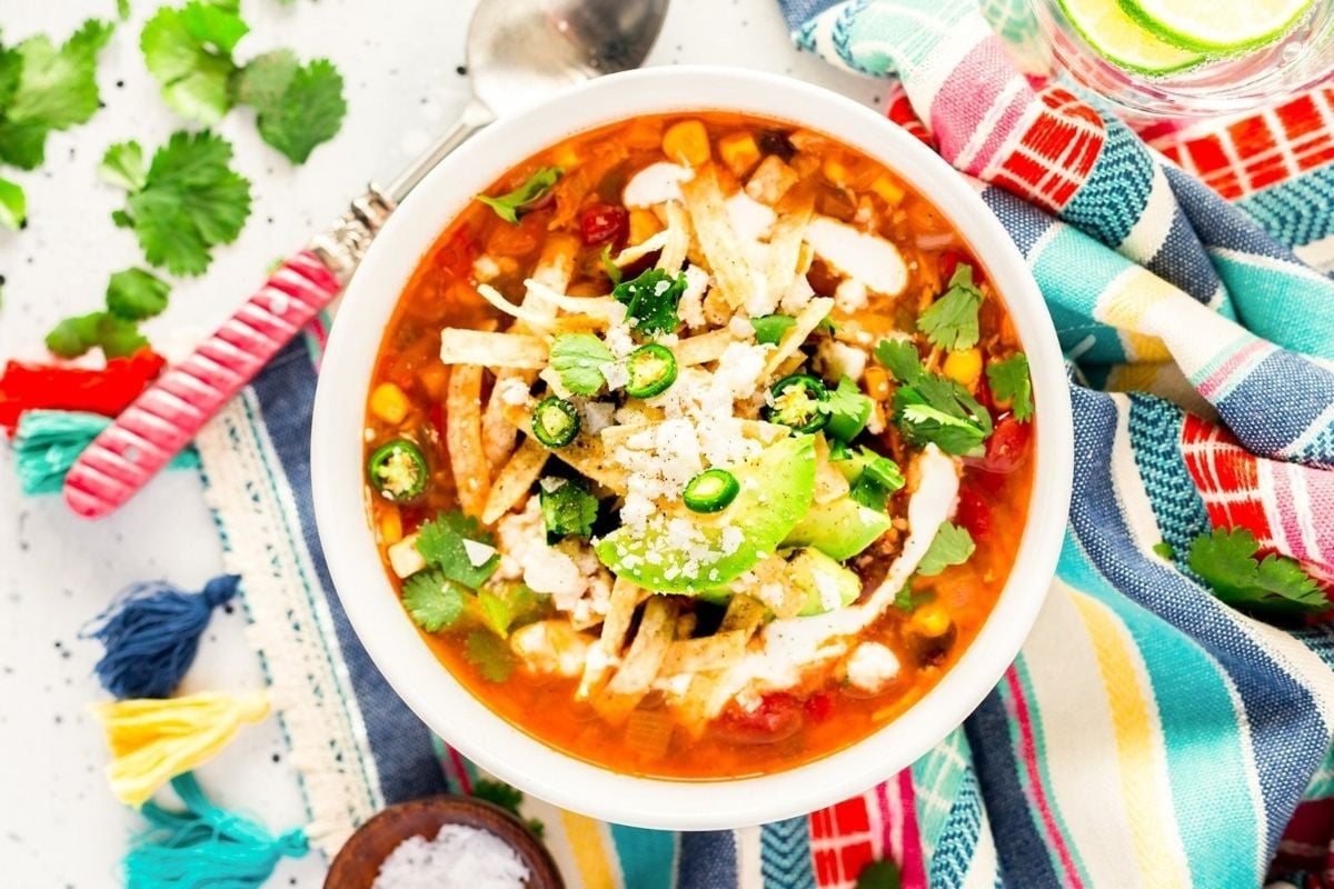 A bowl of tomato-based mexican chicken soup on a colorful tablecloth.