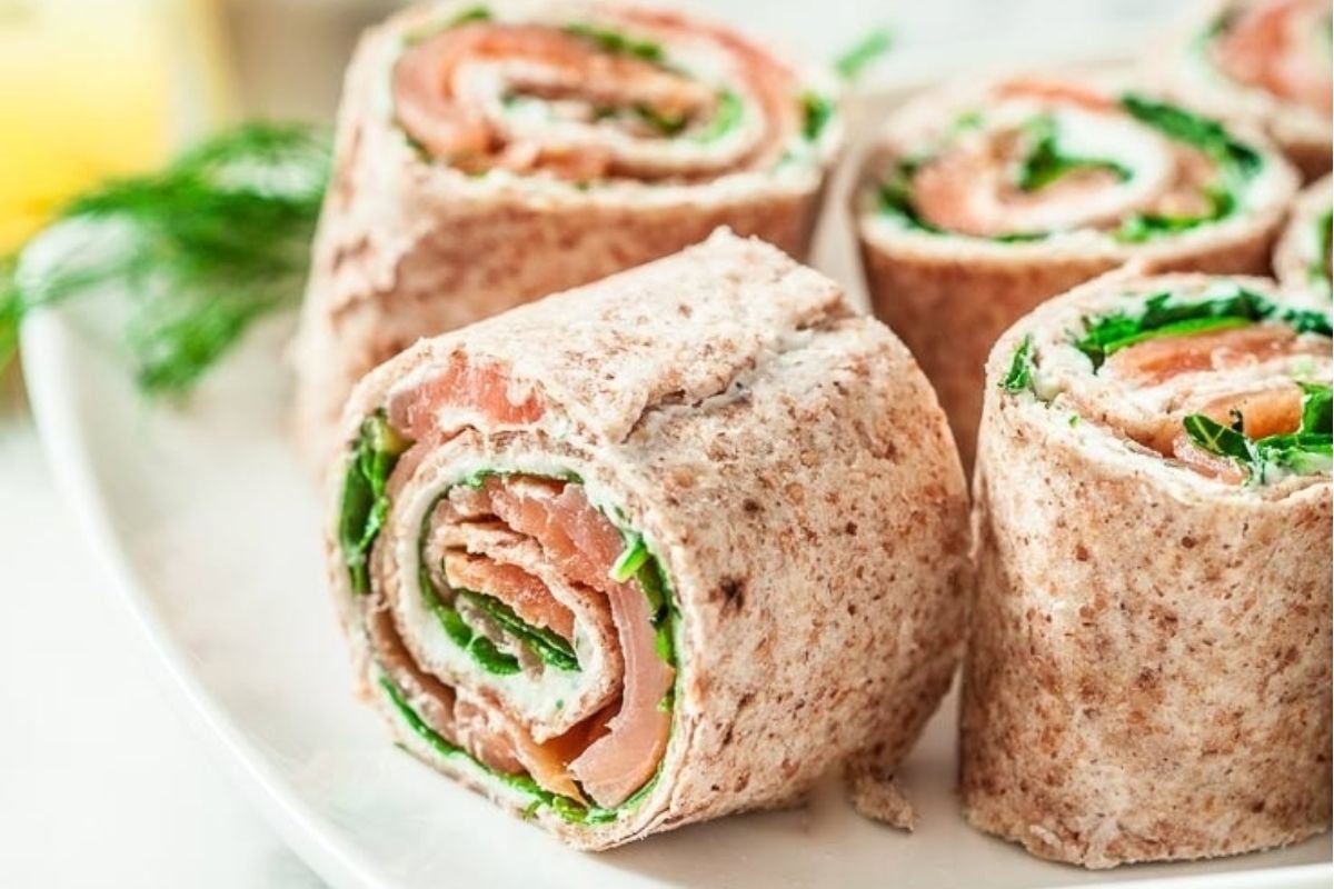 Plate of smoked salmon and cream cheese pinwheel recipes with greens on a white plate.