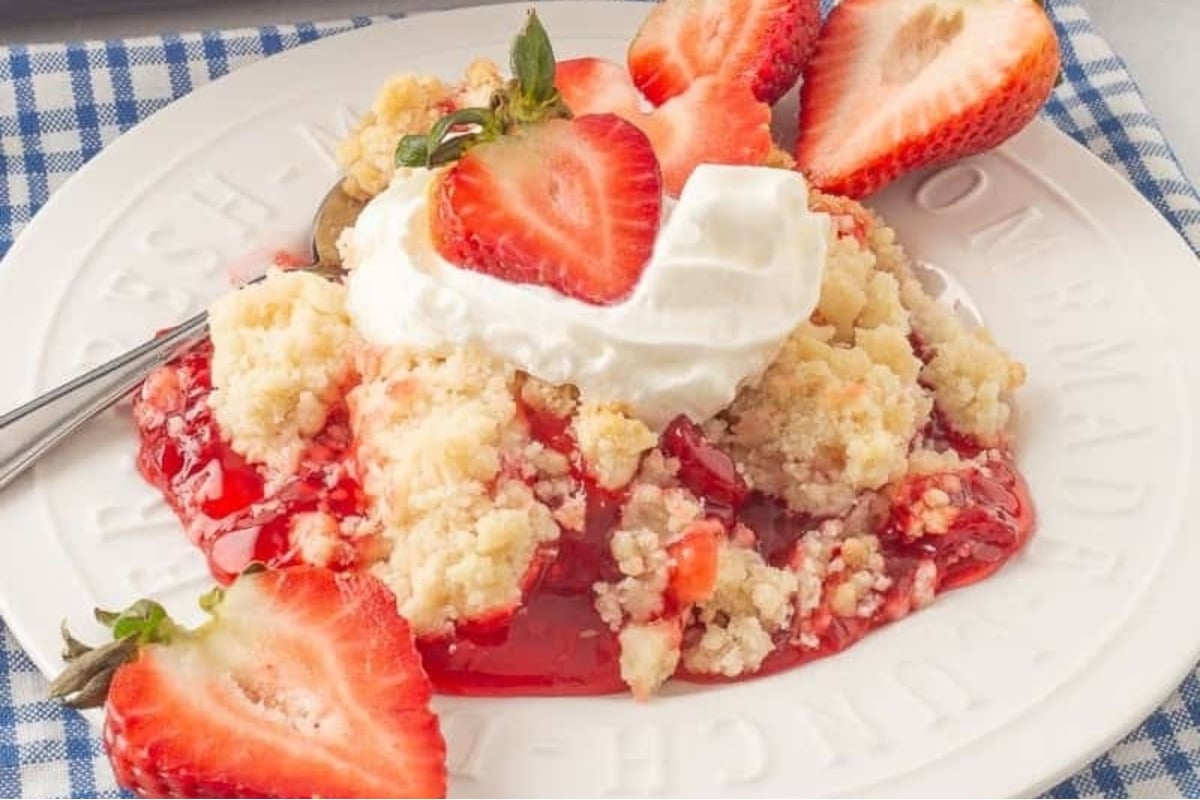 Strawberry dump cake on a white plate with whipped cream.