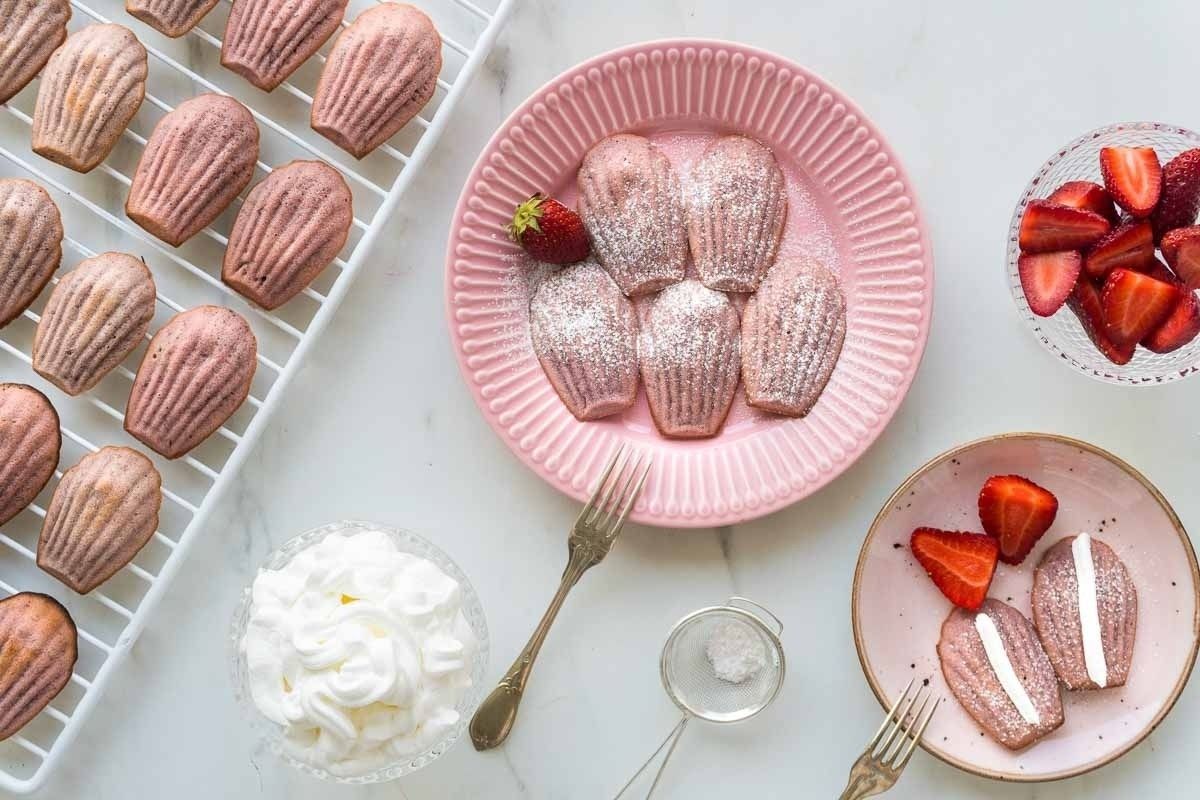Pink macarons with whipped cream and strawberries on a plate.