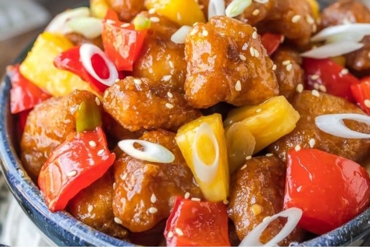 Close-up of sweet and sour chicken with red bell peppers, pineapple, sesame seeds, and sliced green onions—perfect for adding to your collection of Lunar New Year recipes.