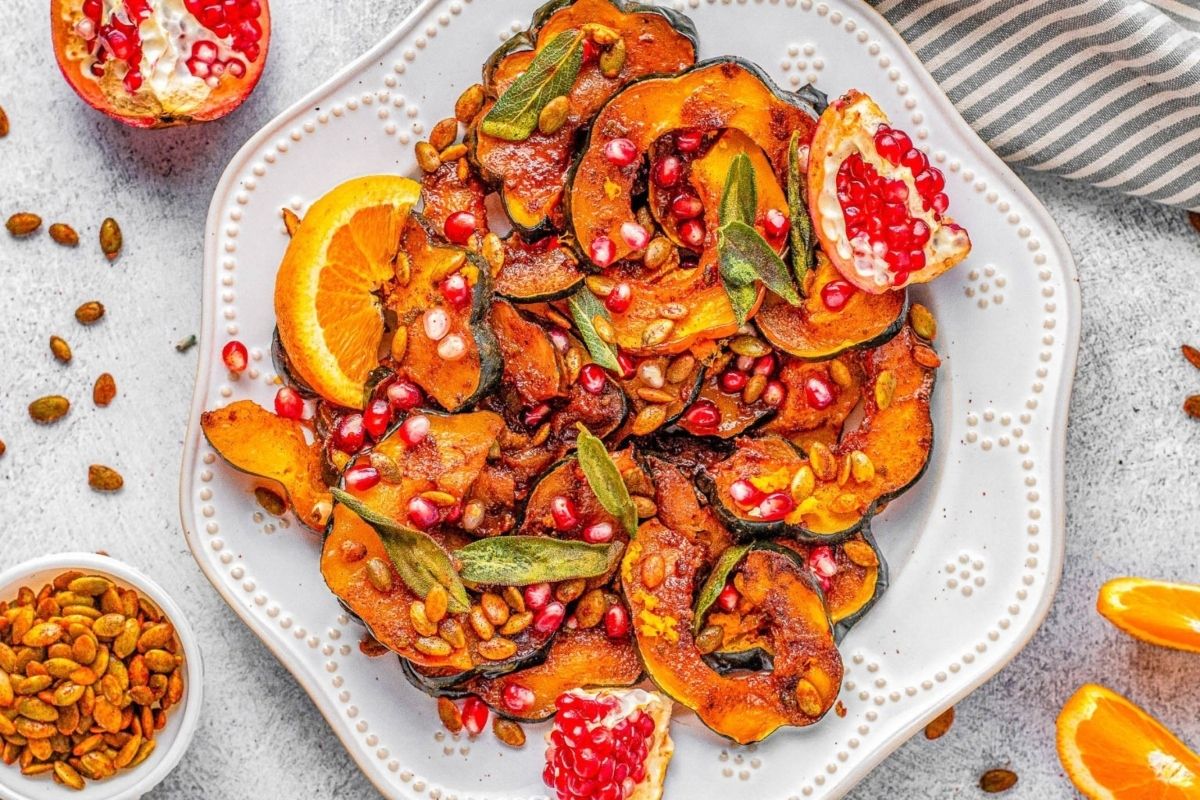 Roasted squash with pomegranate seeds, orange slices, and herbs on a white plate, with pepitas on the side—a vibrant addition to your Lunar New Year recipes.