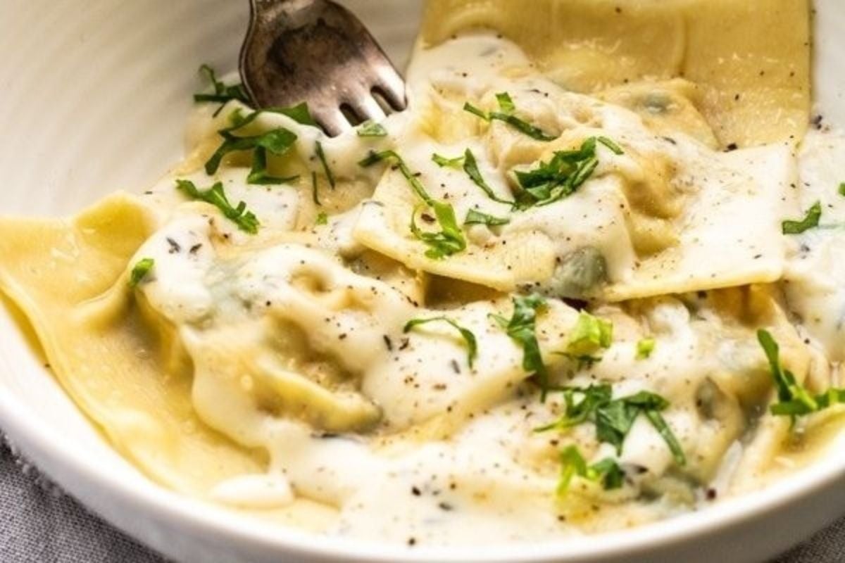 Cheesy ravioli in a white bowl ready to eat with a fork.