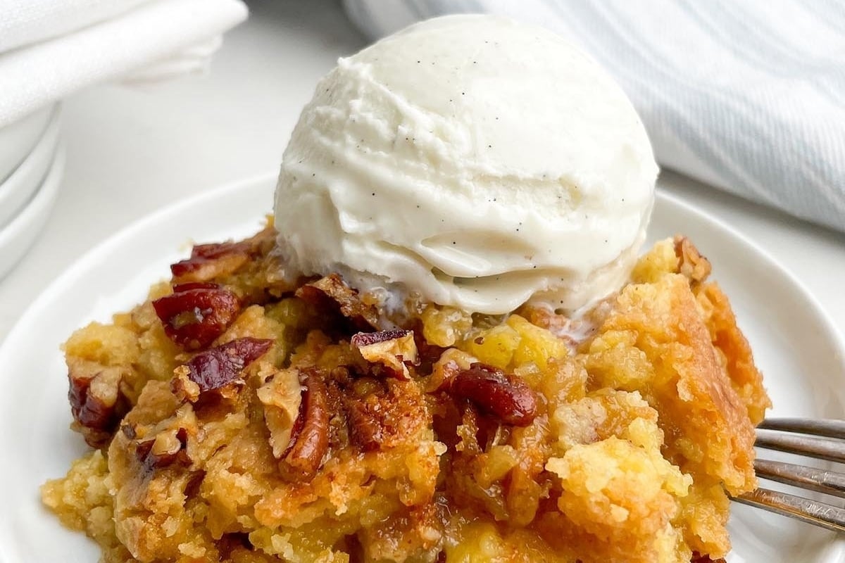 A plate of pecan cobbler with ice cream and pecans, a delicious dessert that is reminiscent of classic dump cakes.