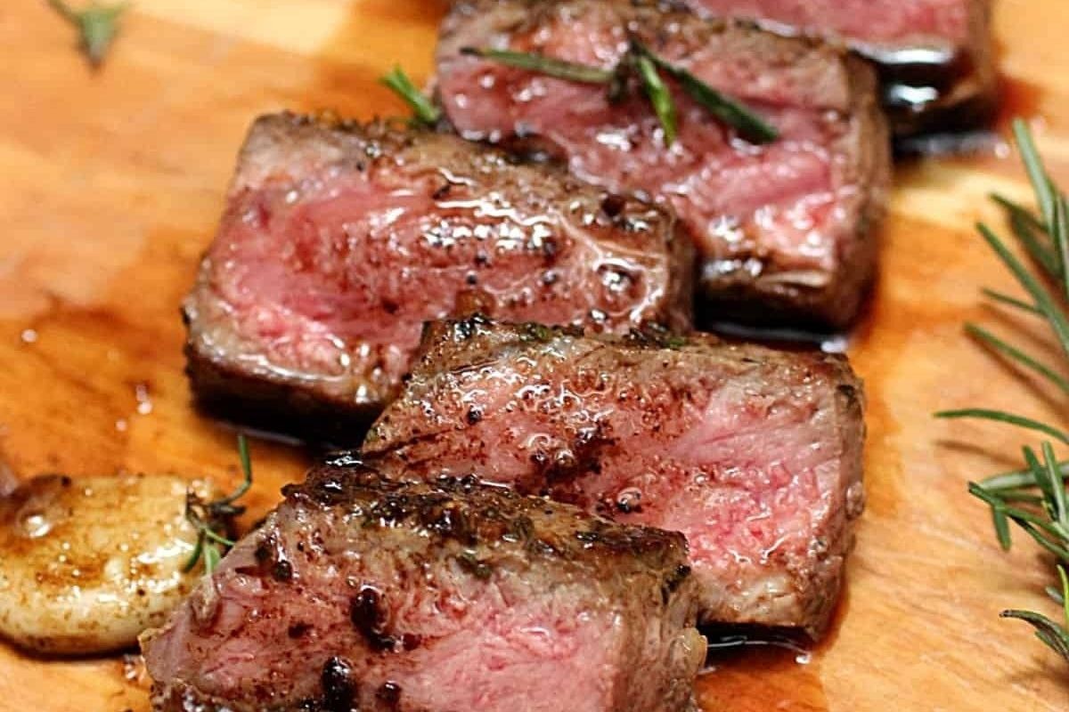 Juicy medium-rare steak slices on a wooden board, garnished with rosemary and garlic—perfect for a romantic Valentine's Date Night Dinner.