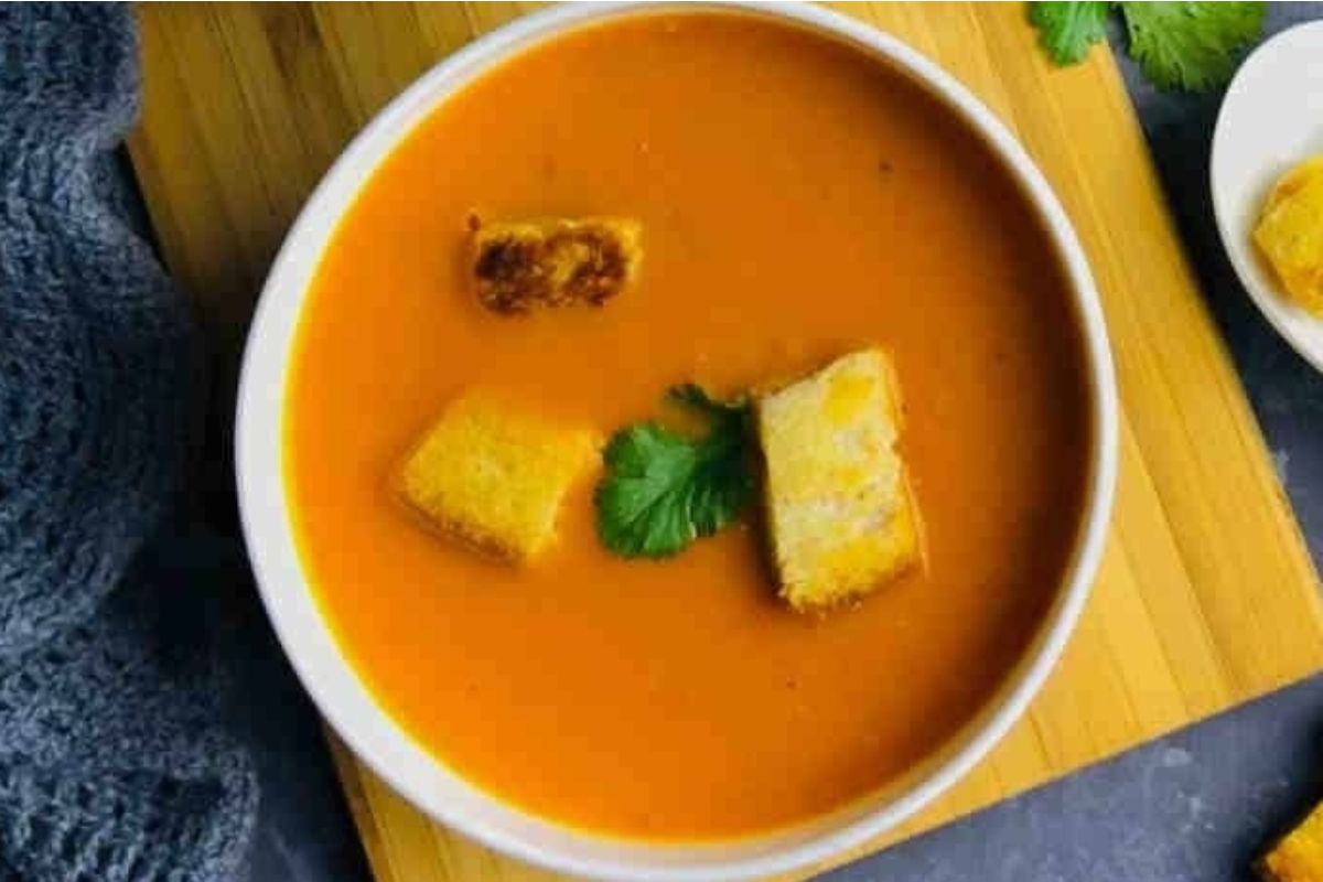 A bowl of tomato soup with croutons on a wooden cutting board, perfect for tomato-based soup recipes.
