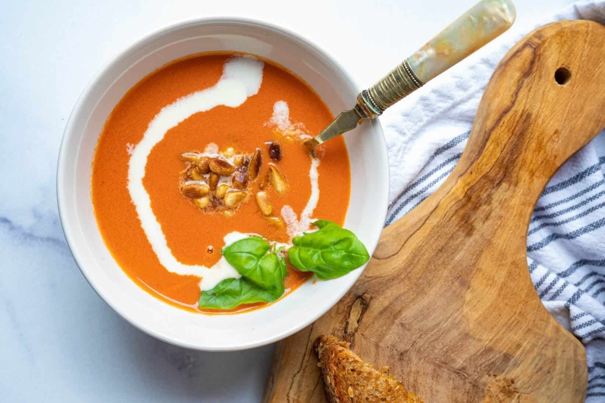A creamy bowl of tomato soup on a wooden cutting board.