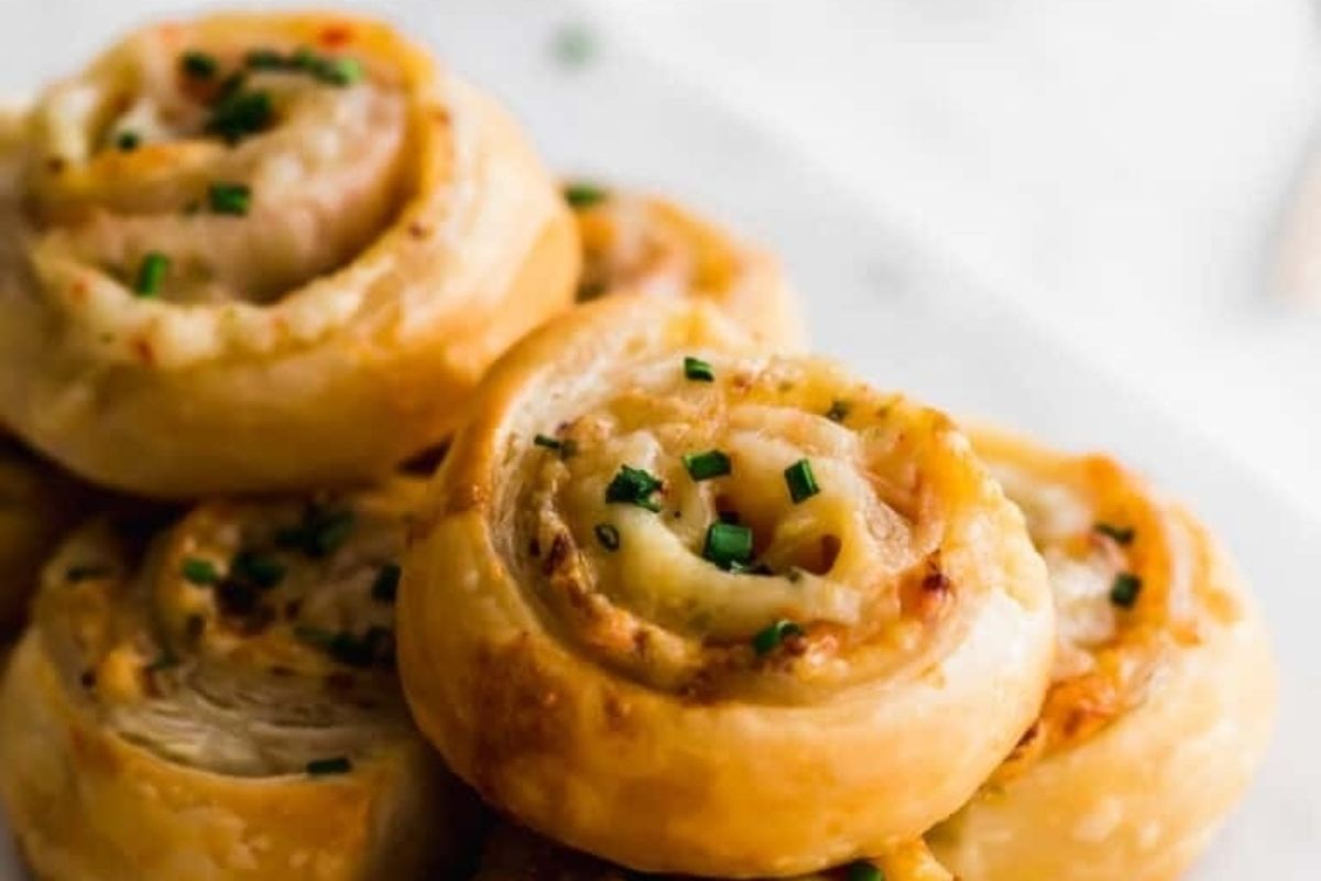 Close-up of golden, flaky pastries from delicious pinwheel recipes, topped with chopped chives on a white plate.