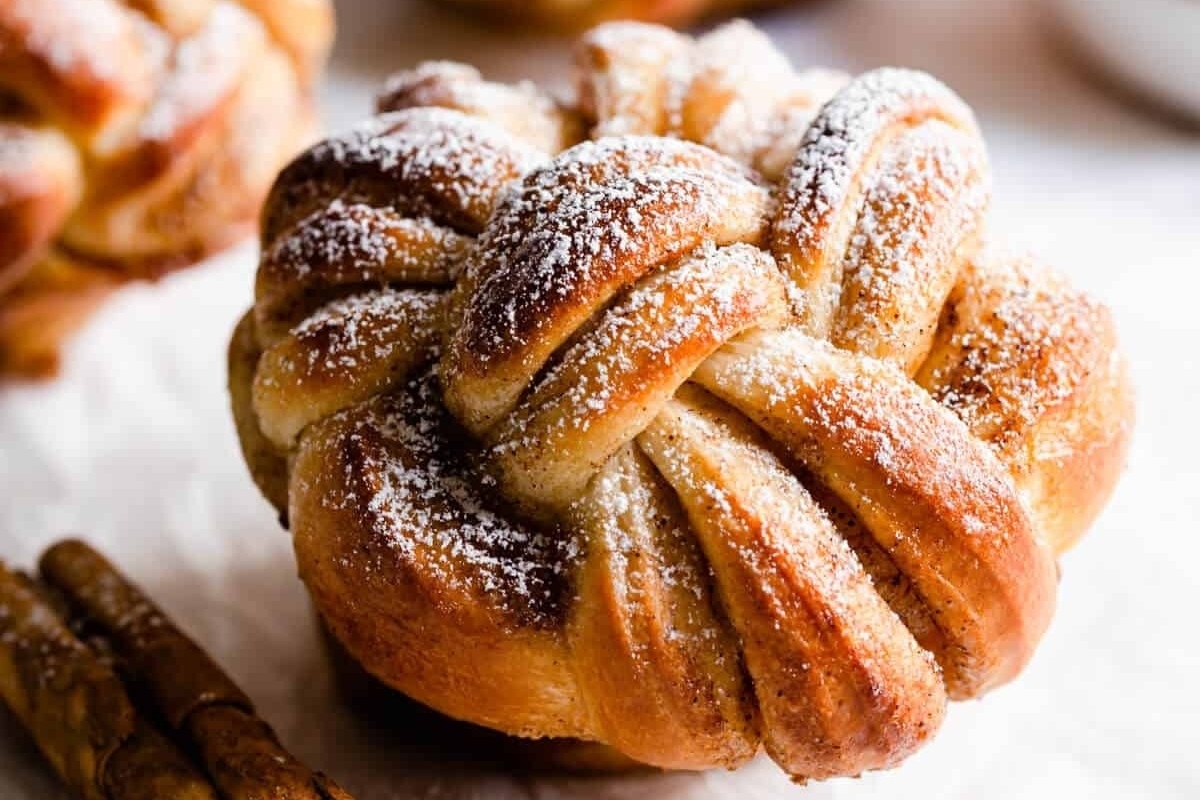 Delicious cinnamon buns adorned with powdered sugar and cinnamon sticks, prepared using mouthwatering cinnamon roll recipes.