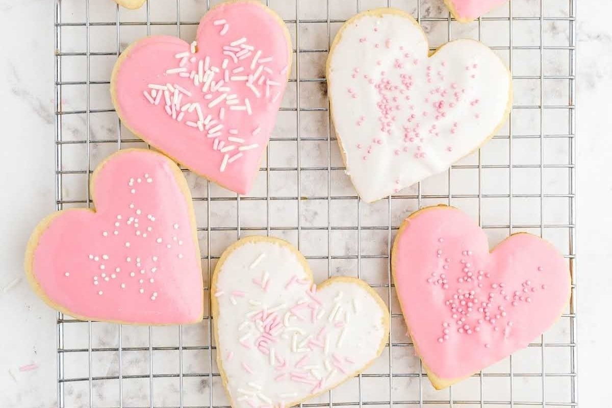 Heart-shaped cookies with pink and white icing and sprinkles on a cooling rack make adorable cute valentine's treats.