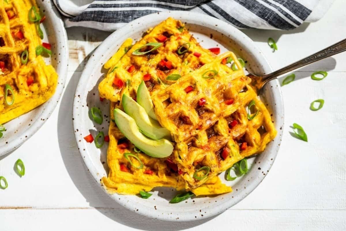 Two plates of waffles with mouthwatering toppings on a white background.