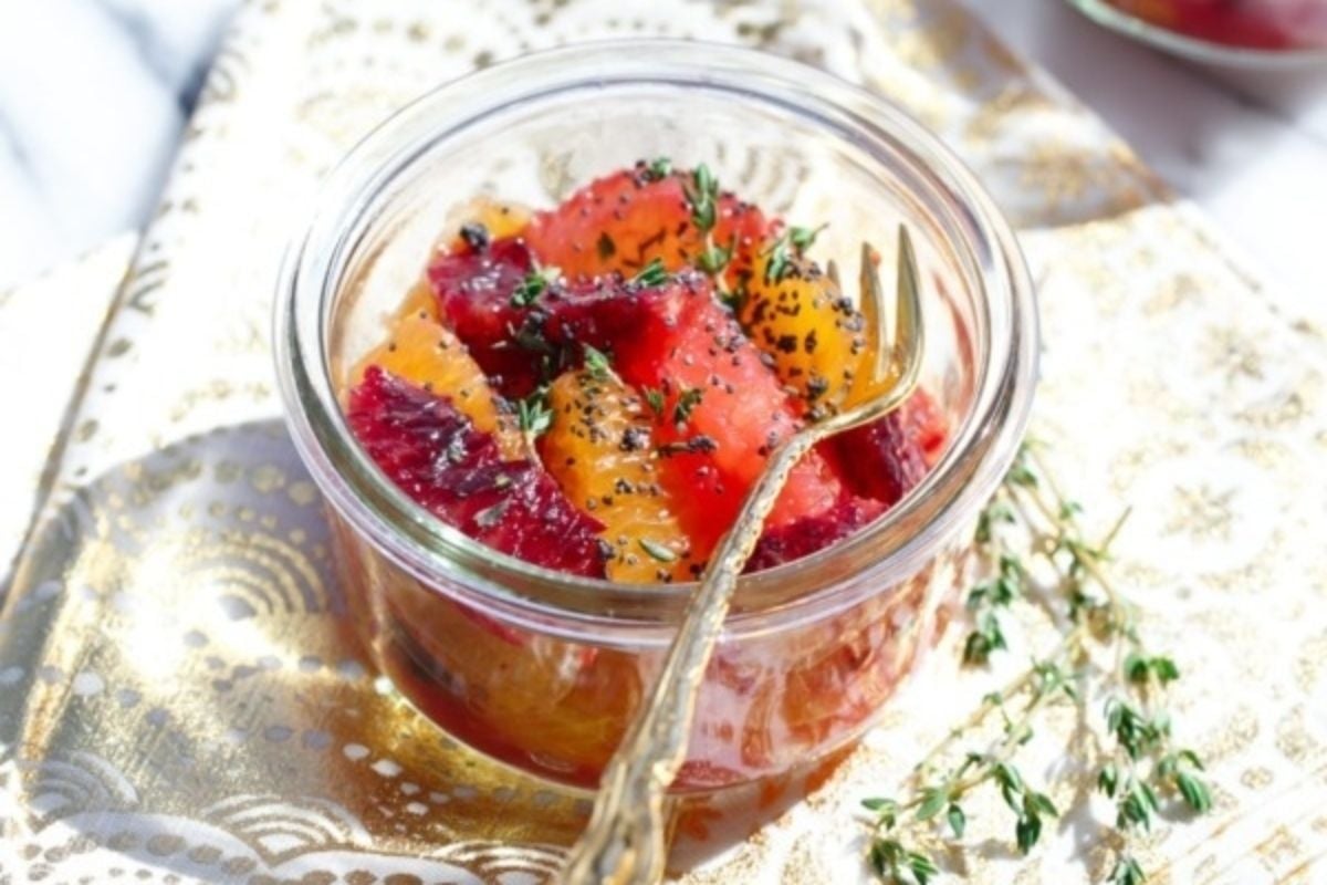 A jar of blood oranges with thyme sits on a table near citrus recipes.